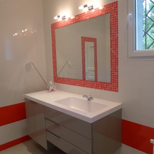 image d'un meuble de salle de bain gris avec plan vasque blanc, le miroir est entouré d'une mosaïque rouge